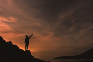 silhouette photography of person standing on rock beside body of water